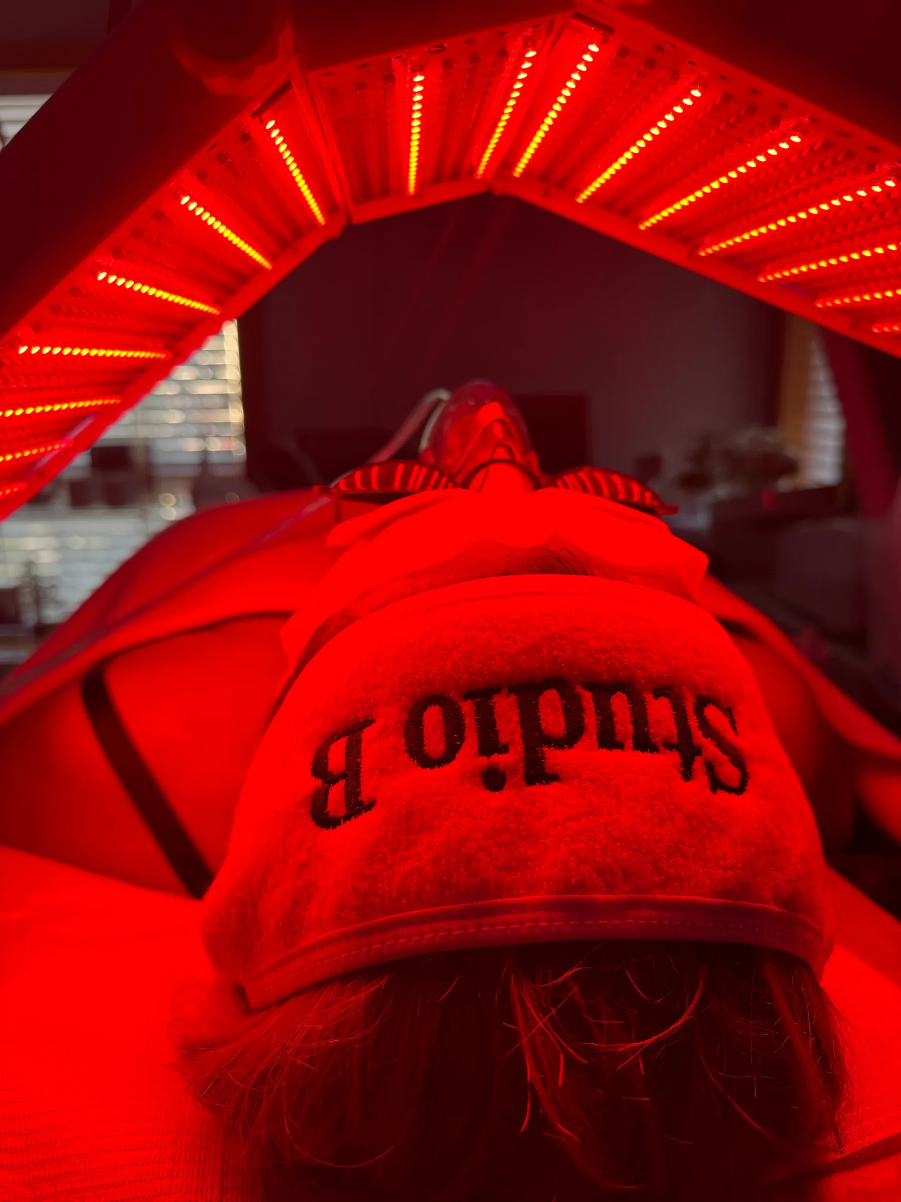 Una clienta bajo el domo de luz LED roja de Studio B, con una toalla bordada con el nombre del estudio