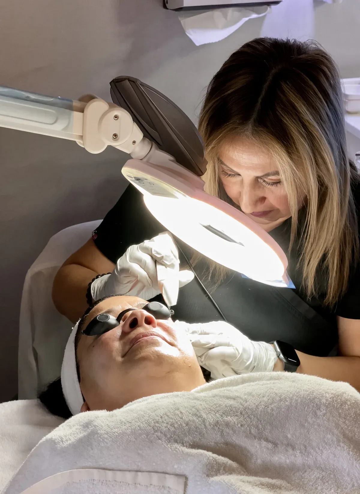 A Studio B specialist checks a client's skin under a magnifying lamp